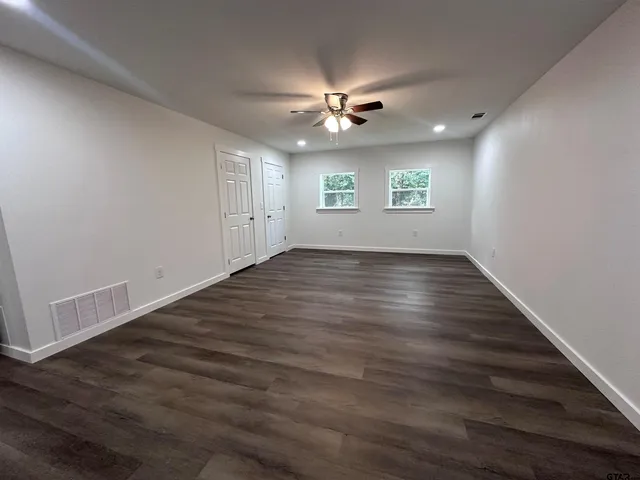 an empty room with wooden floor ceiling fan and windows