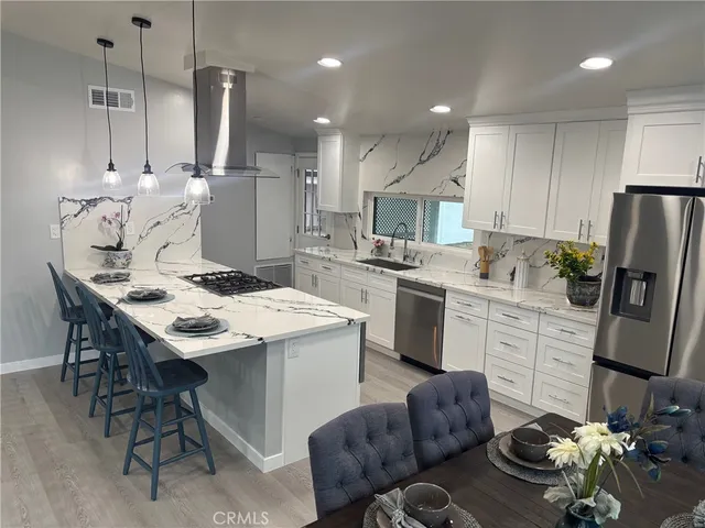 a kitchen with stainless steel appliances kitchen island granite countertop a sink a stove a refrigerator and white cabinets with wooden floor