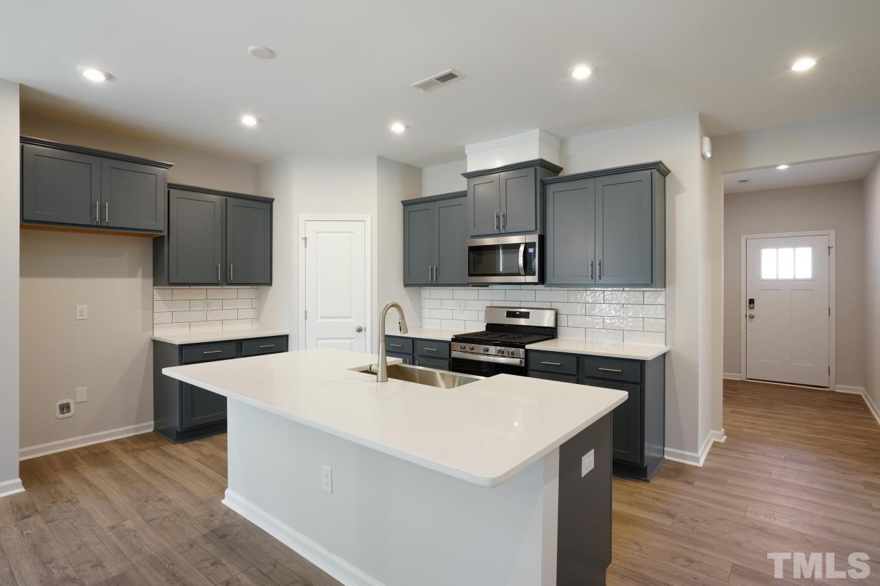 393 Madden Rose Loop Garner, NC 27529 - Photo 3 of 31 a kitchen that has a sink a microwave oven a stove and a center island with wooden floor