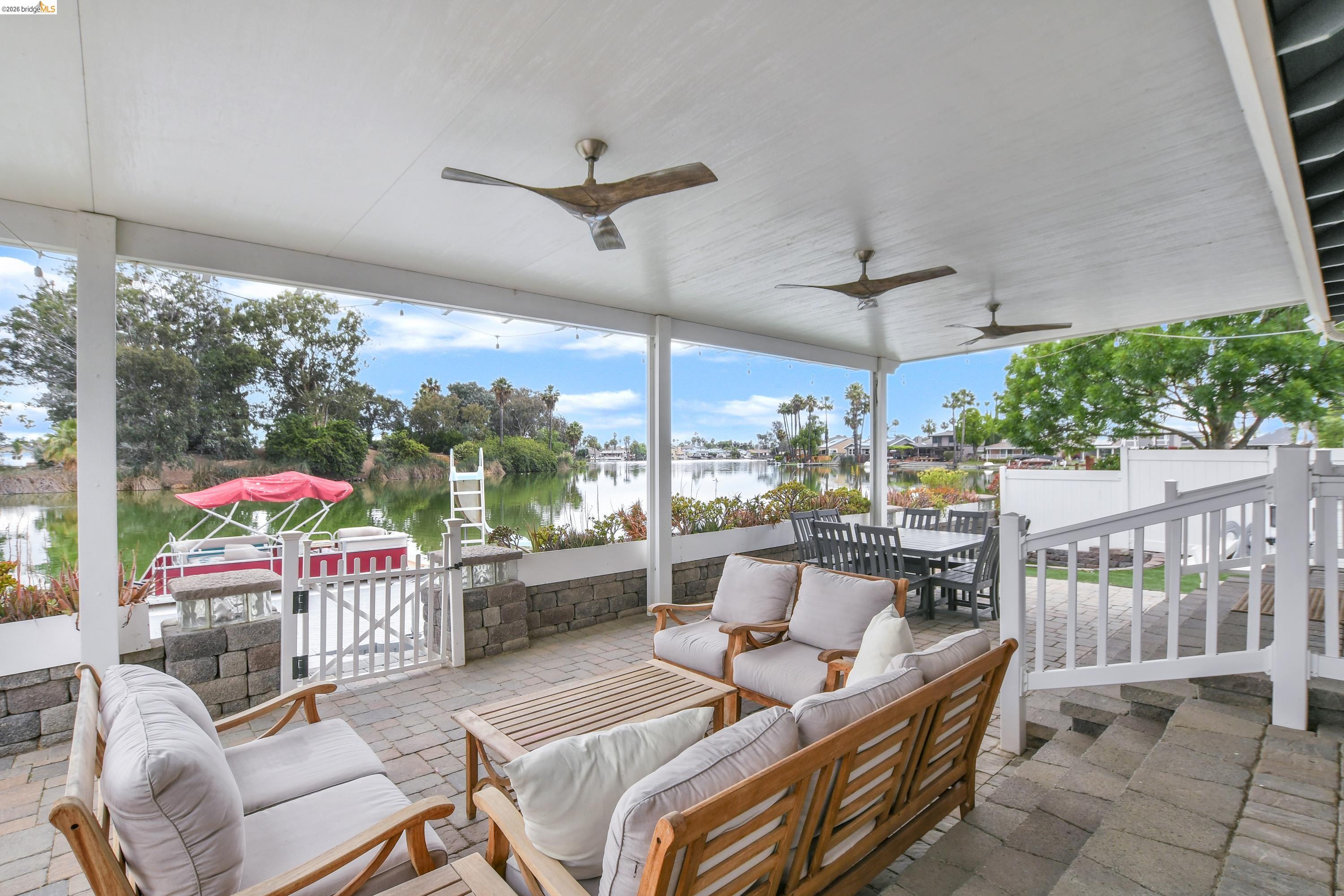 1432 Willow Lake Road Discovery Bay, CA 94505 - Photo 32 of 40 Covered outdoor patio featuring a paver stone surface, multiple ceiling fans, a waterfront setting, and an adjacent boat dock with a white gate