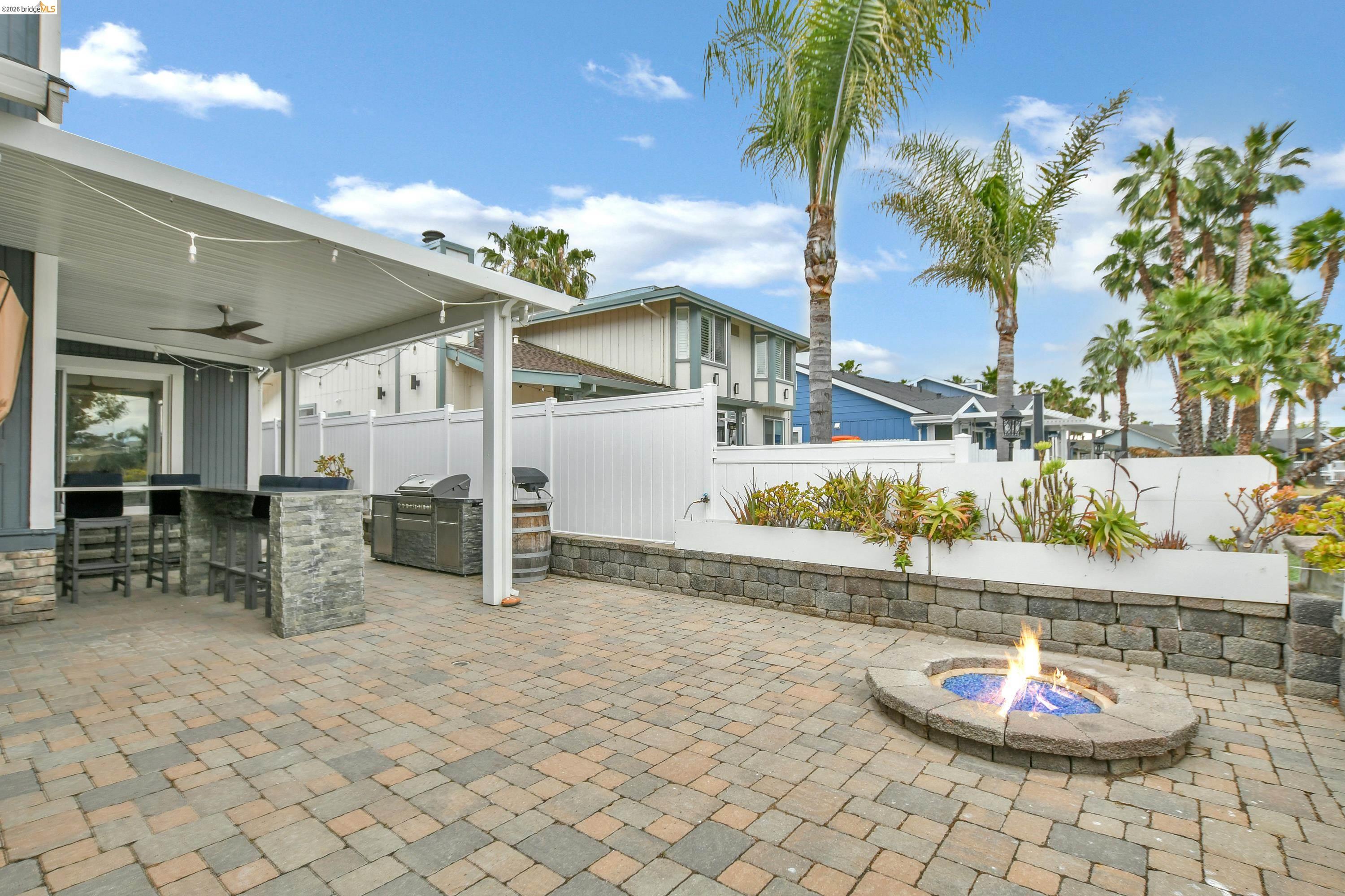 1432 Willow Lake Road Discovery Bay, CA 94505 - Photo 37 of 40 Expansive paver patio featuring a built-in fire pit, covered outdoor dining area with integrated bar seating, and a stone-clad planter with established landscaping