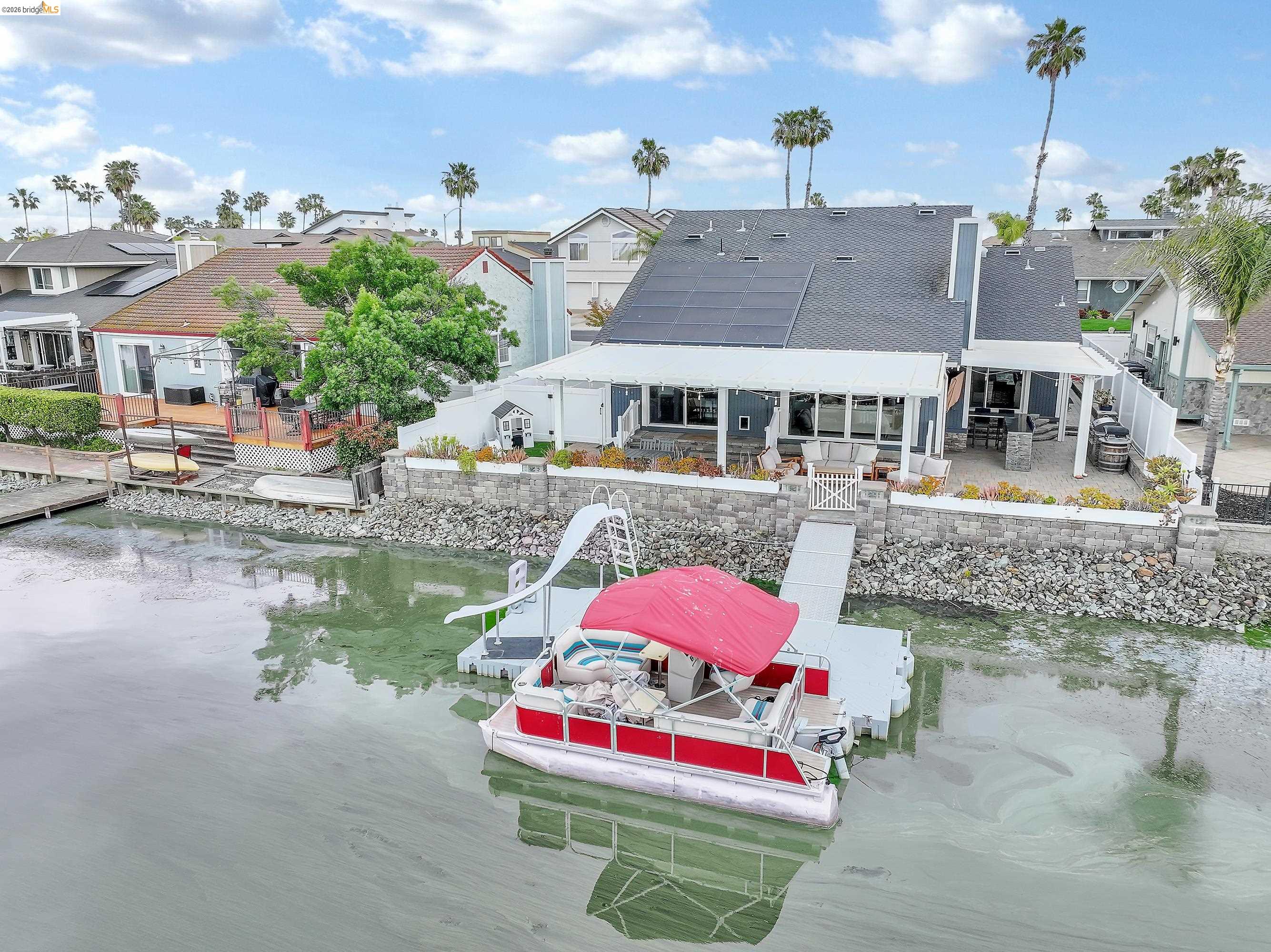 1432 Willow Lake Road Discovery Bay, CA 94505 - Photo 40 of 40 Waterfront property featuring a private dock with an attached slide, extensive patio space, a covered outdoor kitchen area, and solar panels on the roof
