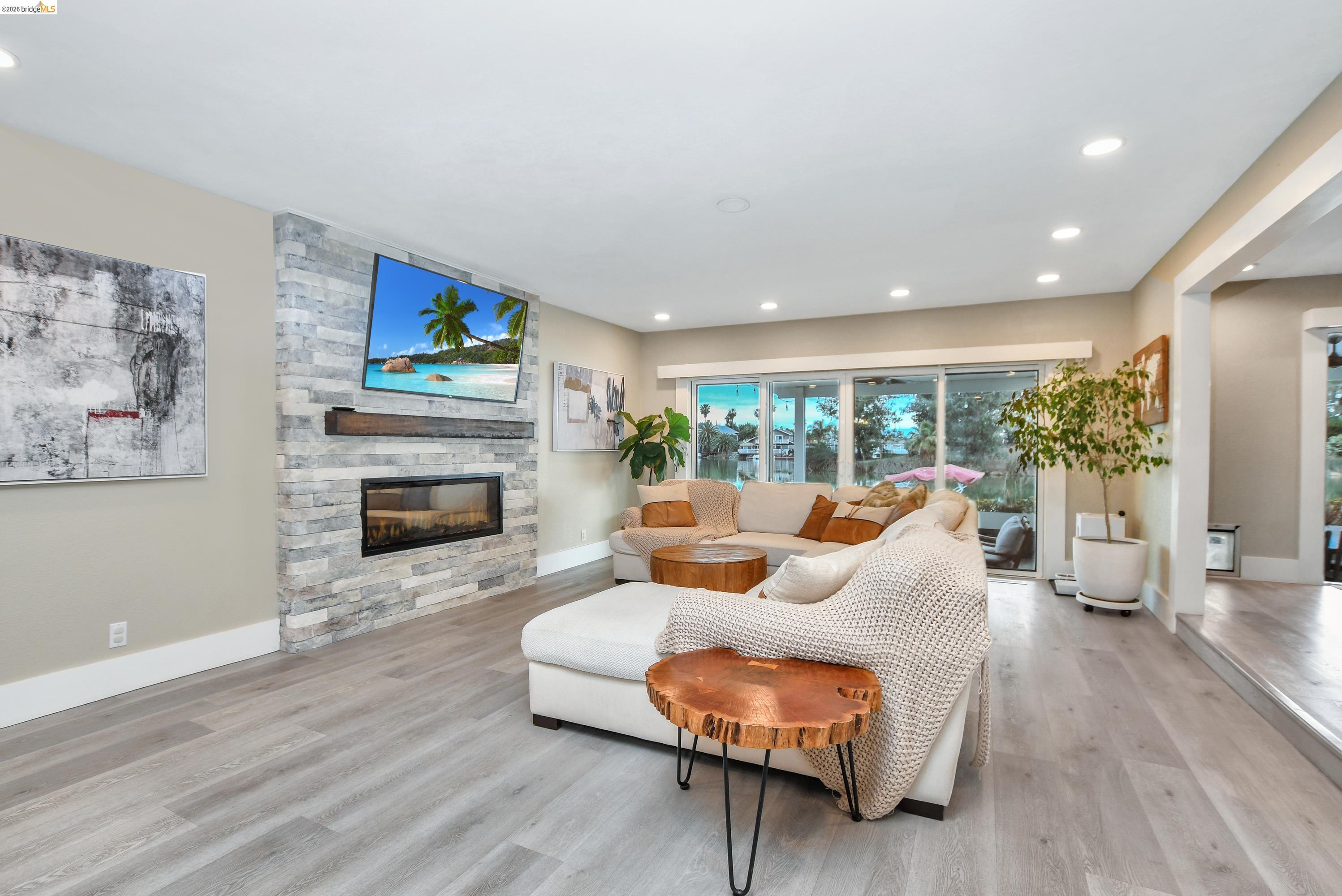 1432 Willow Lake Road Discovery Bay, CA 94505 - Photo 9 of 40 Living area featuring light wood-finish flooring, a stacked stone fireplace with an integrated linear firebox, a dark wood mantel, recessed ceiling lighting, and expansive glass sliding doors
