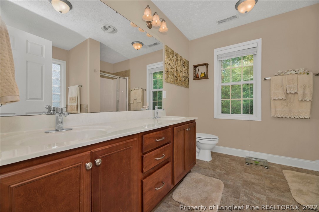 723 Cape Fear Road Raeford, NC 28376 - Photo 27 of 33 a bathroom with a granite countertop sink a toilet a mirror a window and a shower