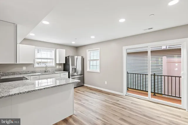 a view of a kitchen with granite countertop wooden floor a counter top space and stainless steel appliances