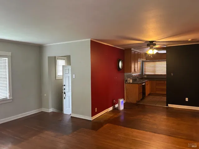 an empty room with kitchen view and wooden floor