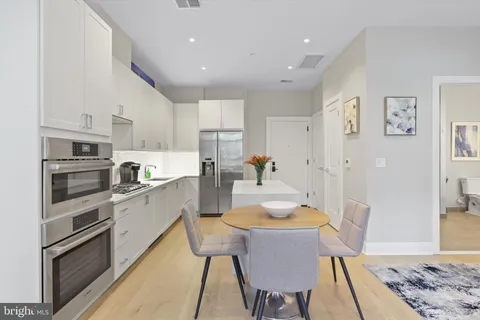 a kitchen with stainless steel appliances granite countertop a stove top oven a refrigerator a dining table and chairs with wooden floor