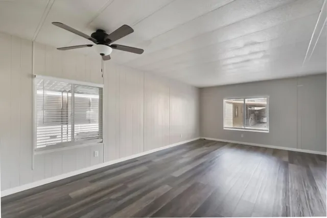 an empty room with wooden floor fan and windows