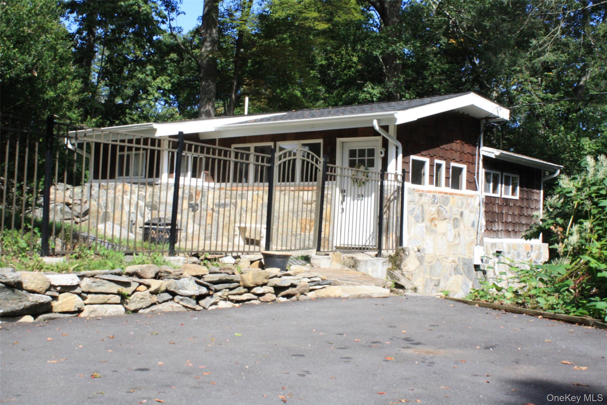View of front of property featuring a fenced front yard, a gate, view of wooded area, and stone siding