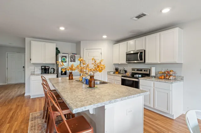 a kitchen with stainless steel appliances granite countertop a stove top oven a sink a dining table and chairs with wooden floor