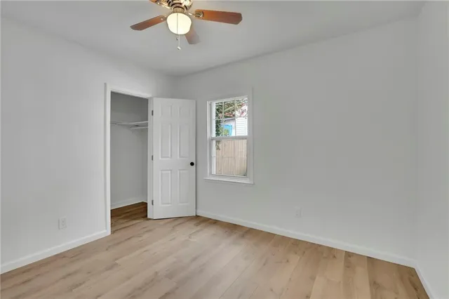 an empty room with wooden floor chandelier fan and windows