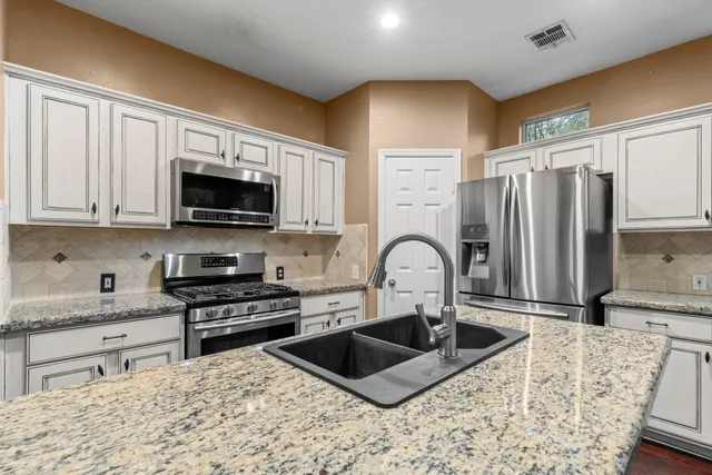 a kitchen with stainless steel appliances granite countertop a sink a stove a refrigerator cabinets and a counter top space