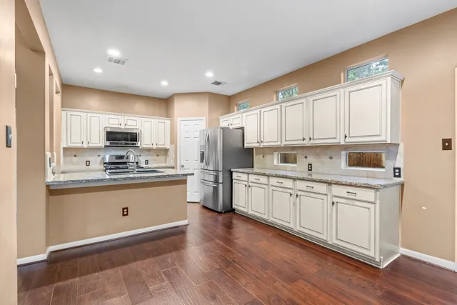 a kitchen with stainless steel appliances granite countertop a refrigerator a sink dishwasher a stove and white cabinets with wooden floor