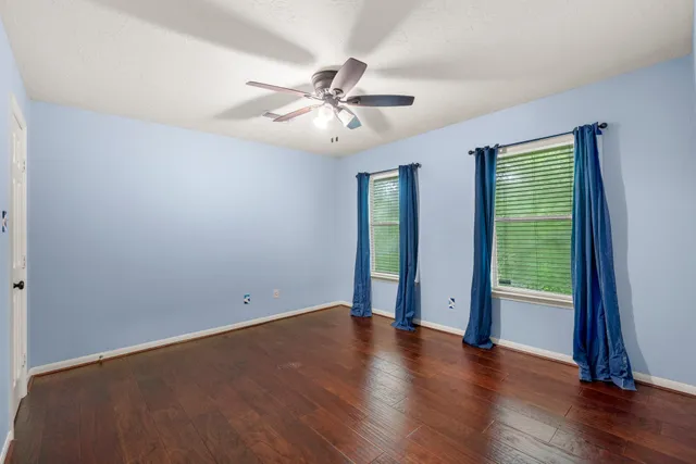 an empty room with wooden floor fan and windows