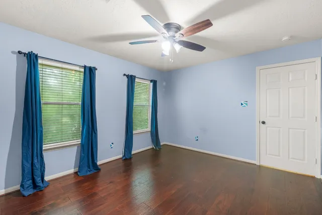 an empty room with wooden floor fan and windows