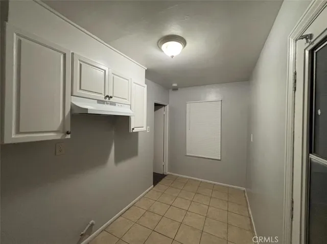 a view of an empty room with kitchen and window