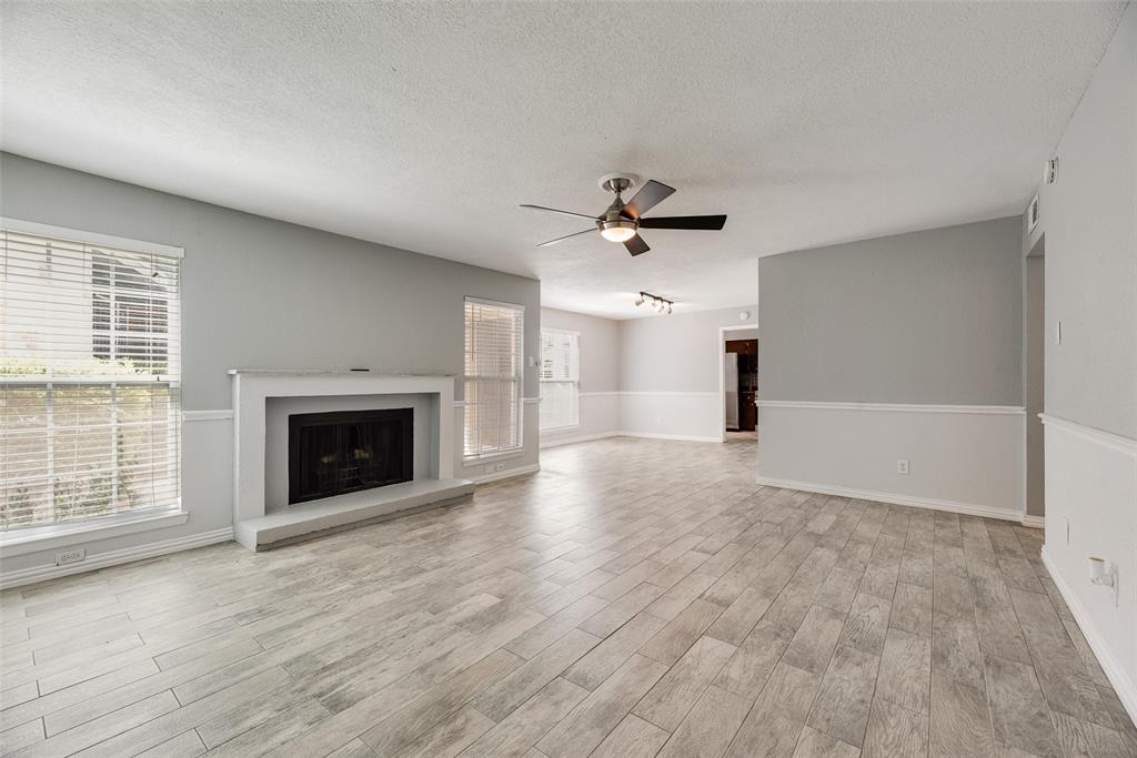 5109 Cedar Springs Road, Unit 105 Dallas, TX 75235 - Photo 4 of 16 Spacious living area featuring a fireplace with a white mantel, light wood-finish flooring, and multiple windows with blinds