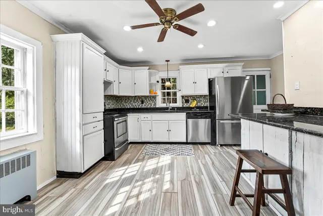 a kitchen with granite countertop a refrigerator oven a sink a stove and white cabinets