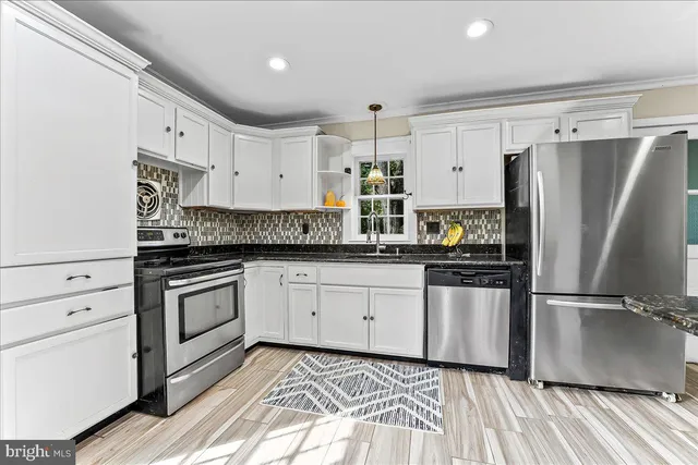 a kitchen with granite countertop a refrigerator oven a sink and white cabinets