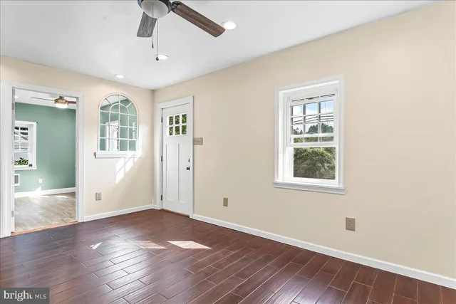 an empty room with wooden floor a ceiling fan and windows