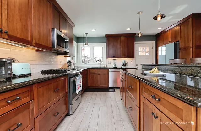 a kitchen with stainless steel appliances granite countertop wooden cabinets a sink dishwasher a stove and a refrigerator