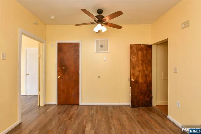 a view of an empty room with wooden floor and a ceiling fan