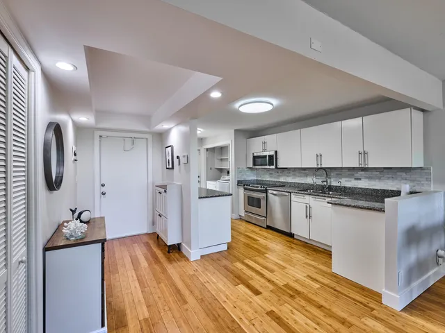 a kitchen with stainless steel appliances granite countertop a stove top oven a sink dishwasher and a refrigerator with wooden floor