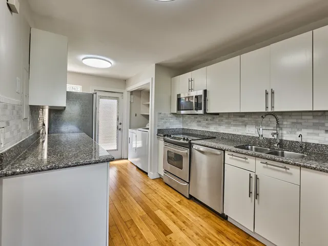 a kitchen with stainless steel appliances granite countertop a sink a stove a refrigerator and white cabinets