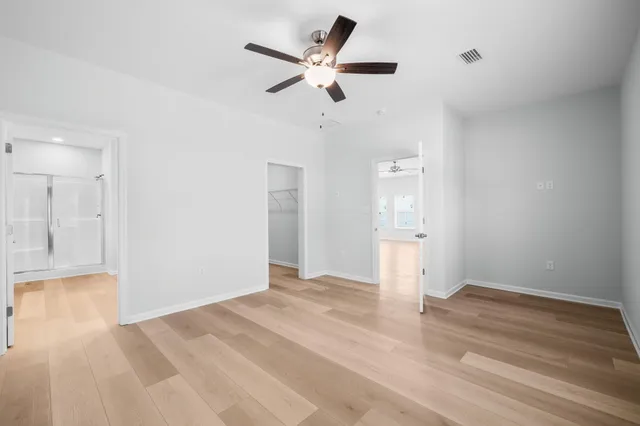a view of an empty room with wooden floor and a ceiling fan