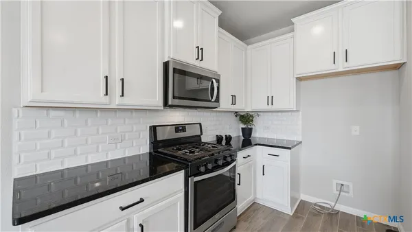 a kitchen with stainless steel appliances granite countertop white cabinets a stove a microwave and a sink