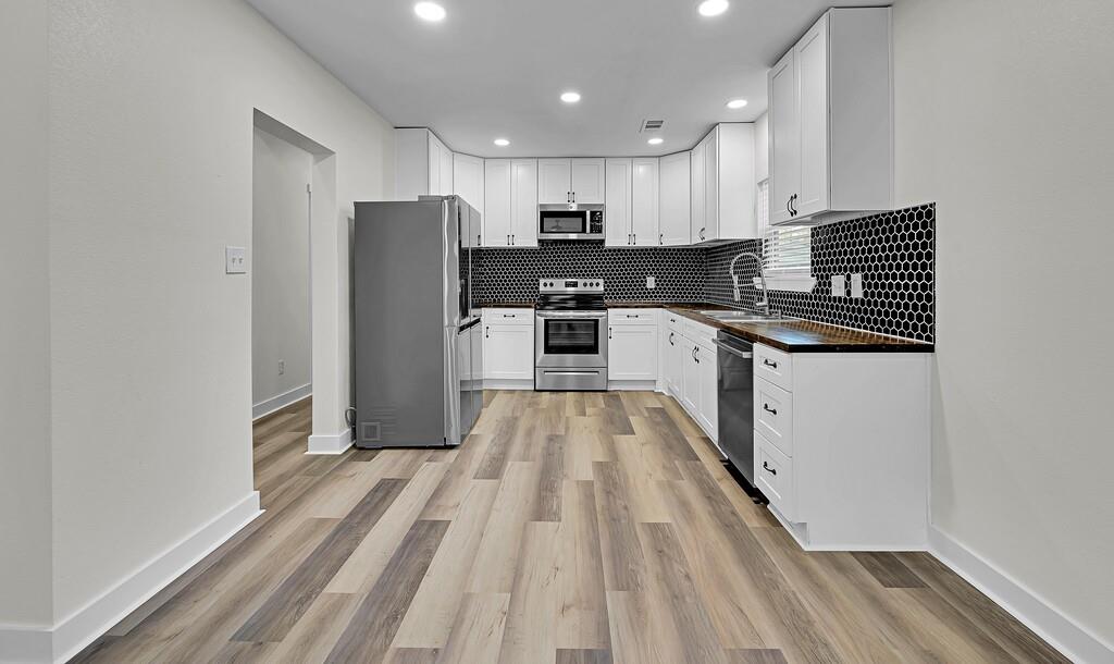 1713 Reuter Avenue Waco, TX 76708 - Photo 7 of 34 Kitchen with appliances with stainless steel finishes, dark countertops, a sink, light wood-style floors, and backsplash
