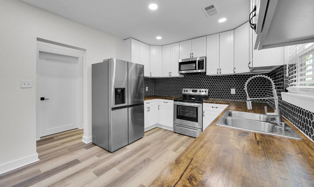 1713 Reuter Avenue Waco, TX 76708 - Photo 8 of 34 Kitchen featuring stainless steel appliances, a sink, backsplash, white cabinetry, and light wood-style flooring