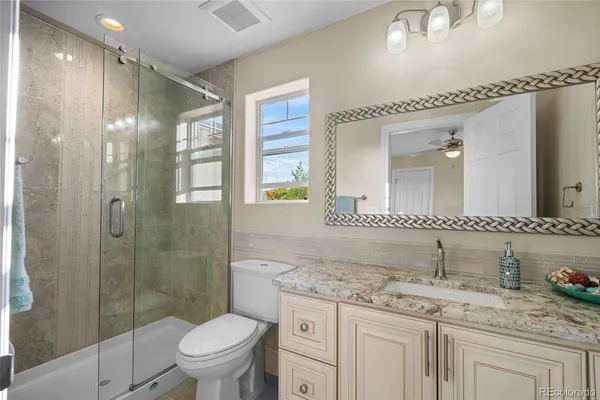 a bathroom with a granite countertop sink a toilet a mirror and shower