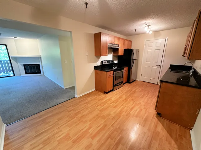 a kitchen with stainless steel appliances kitchen island granite countertop a refrigerator oven a sink dishwasher and white cabinets with wooden floor