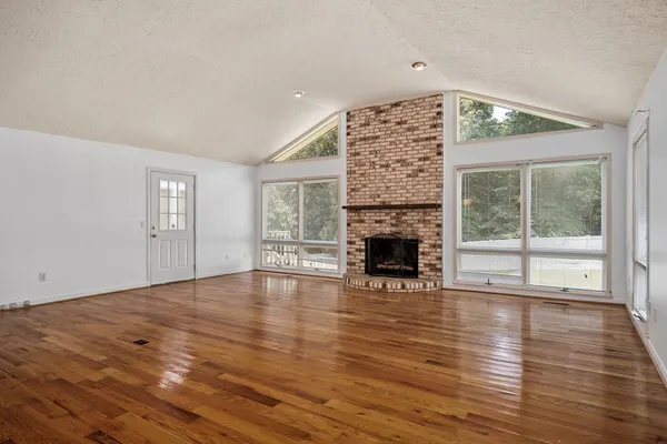 a view of an empty room with wooden floor and a fireplace