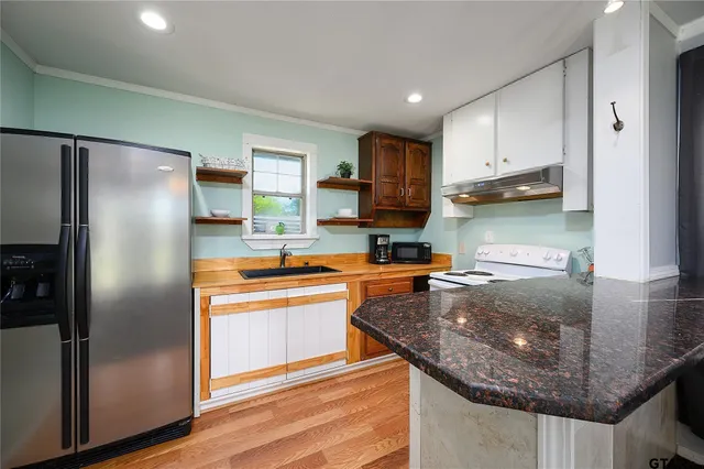 a kitchen with stainless steel appliances granite countertop a refrigerator a stove and a sink with wooden floor