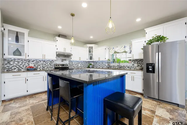 a kitchen with stainless steel appliances kitchen island granite countertop a table chairs stove and refrigerator