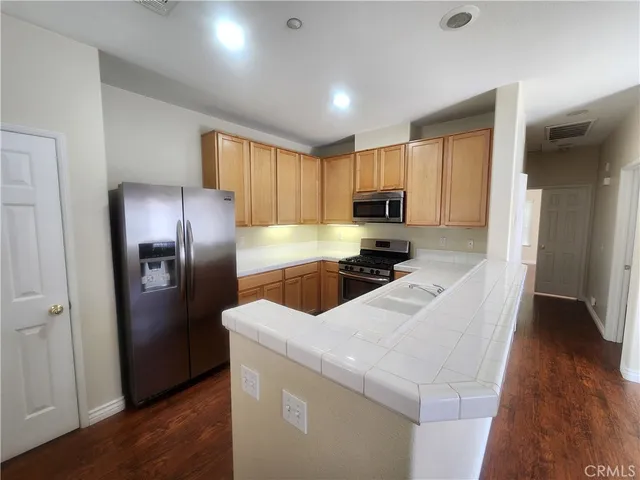 a kitchen with stainless steel appliances kitchen island granite countertop a refrigerator a sink a stove and white cabinets with wooden floor