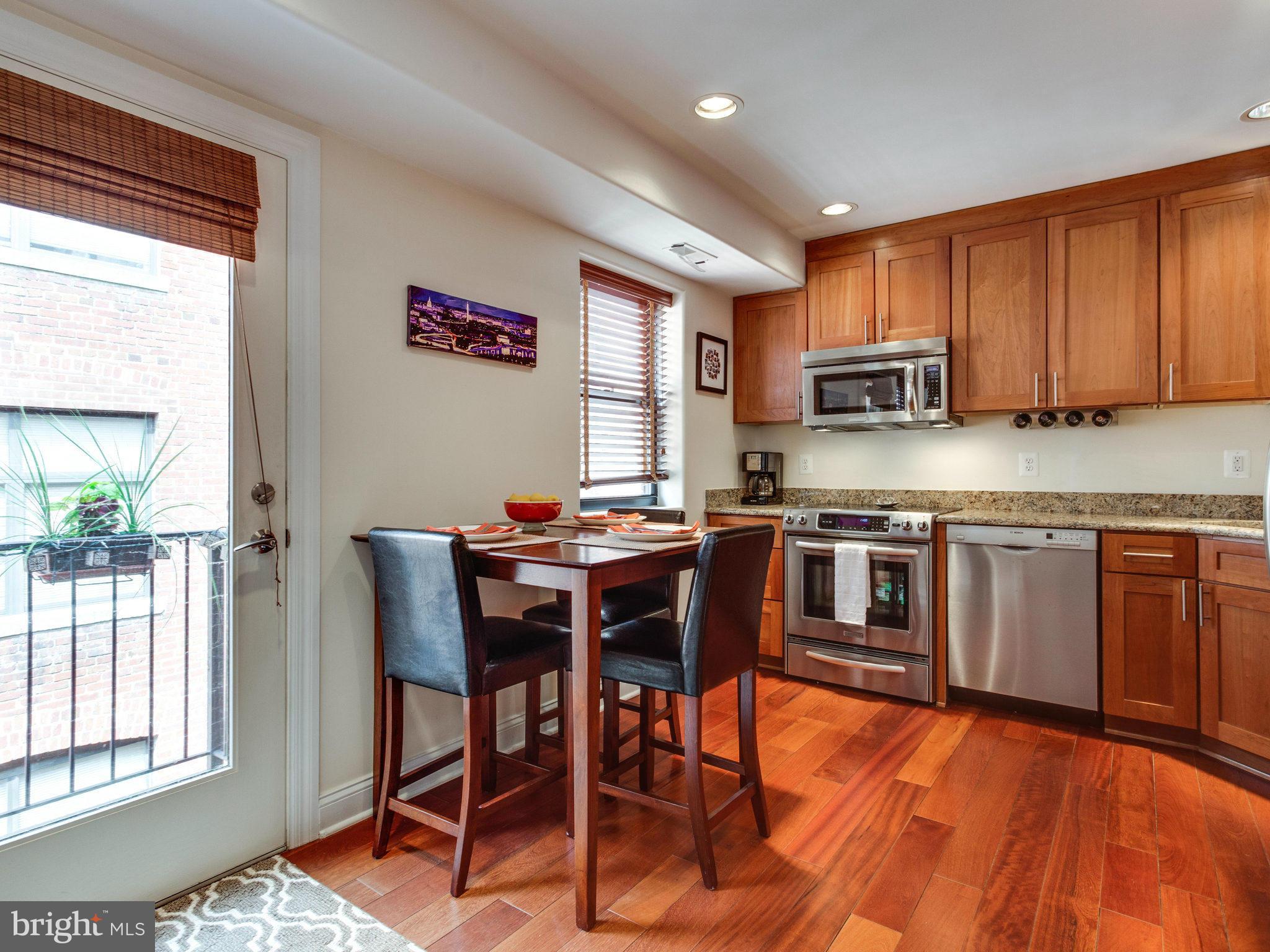 1354 Euclid Street Northwest, Unit B402 Washington, DC 20009 - Photo 8 of 30 a kitchen with stainless steel appliances granite countertop a stove top oven a sink a dining table and chairs with wooden floor