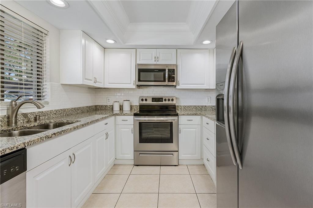 5789 Gage Lane, Unit A 103 Naples, FL 34113 - Photo 6 of 26 a kitchen with white cabinets and stainless steel appliances
