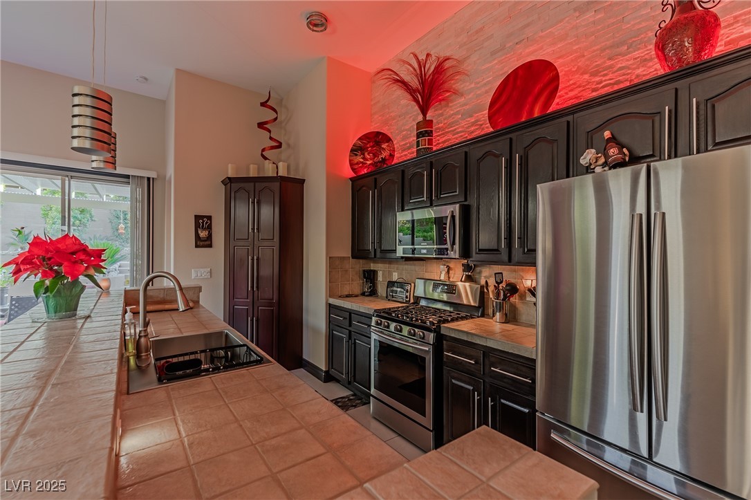17 Chatmoss Road Henderson, NV 89052 - Photo 37 of 58 Kitchen with appliances with stainless steel finishes, backsplash, a sink, tile countertops, and a high ceiling