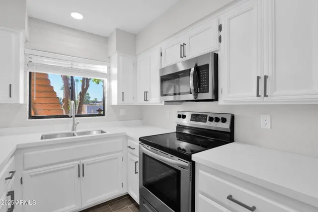 a kitchen with white cabinets appliances a sink and a window
