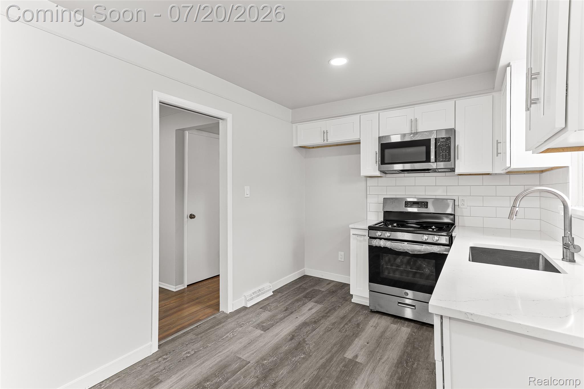 7884 Pardee Road Taylor, MI 48180 - Photo 8 of 23 Contemporary kitchen featuring white cabinetry, stainless steel appliances, a white subway tile backsplash, light-toned countertops, and wood-finish flooring