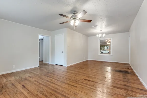 an empty room with wooden floor chandelier fan and windows