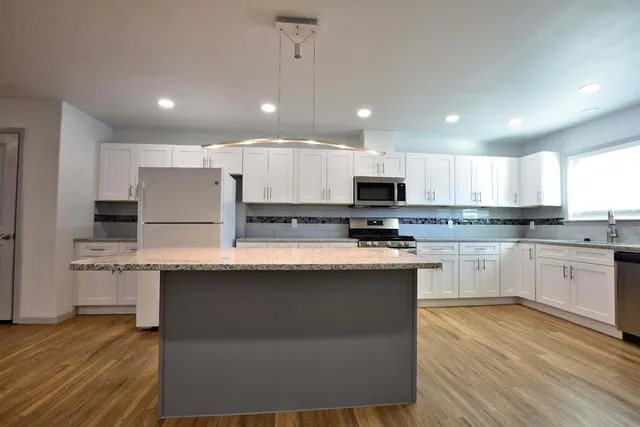 a kitchen with stainless steel appliances granite countertop a stove a sink a refrigerator and white cabinets