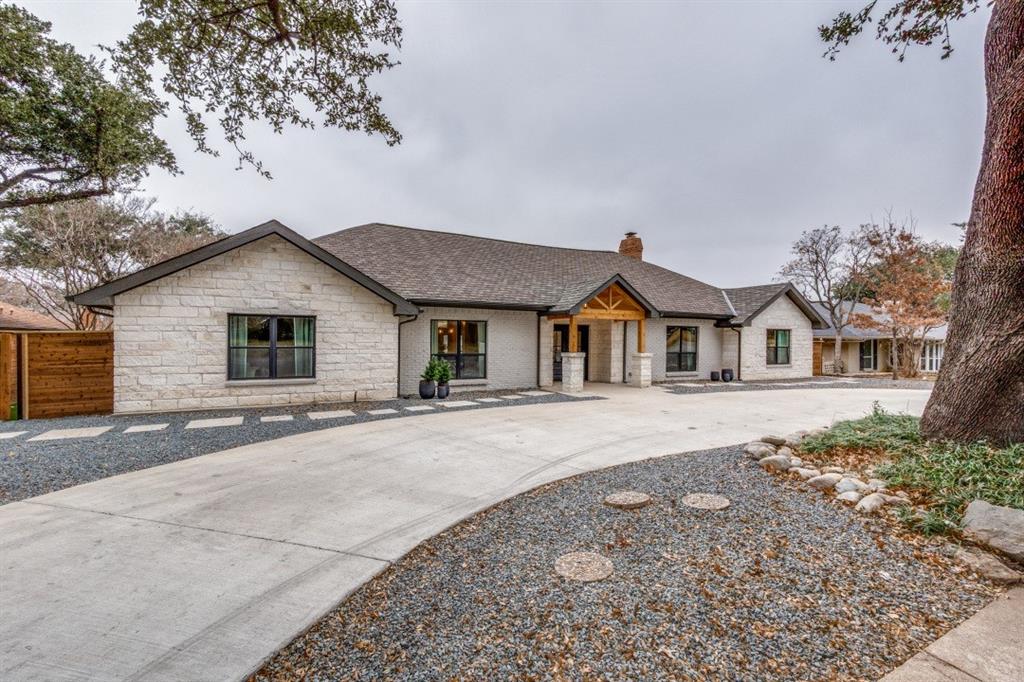 7115 Meadow Road Dallas, TX 75230 - Photo 2 of 22 The property features a stone facade, a dark shingle roof, and an exposed wood entry