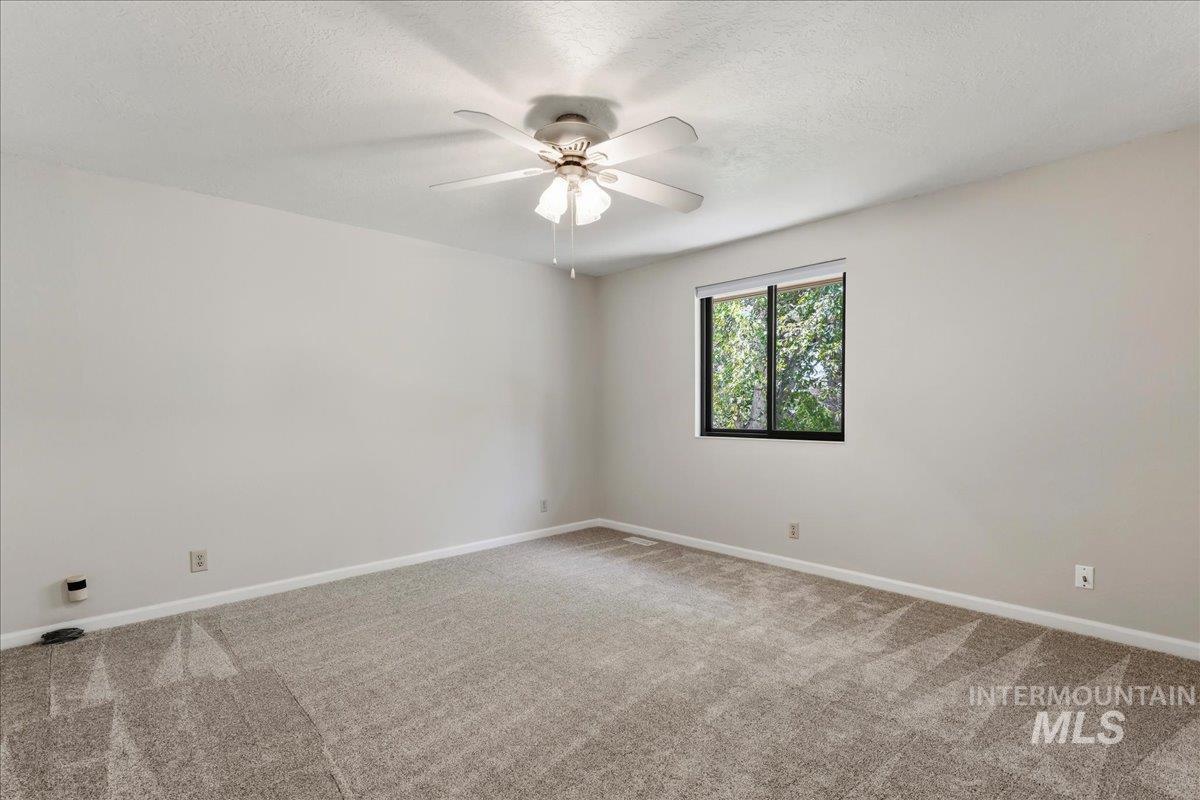 599 Pebble Beach Way Eagle, ID 83616 - Photo 27 of 44 Spacious room featuring neutral carpeting, light-colored walls, a ceiling fan with light fixture, and a window with exterior tree views