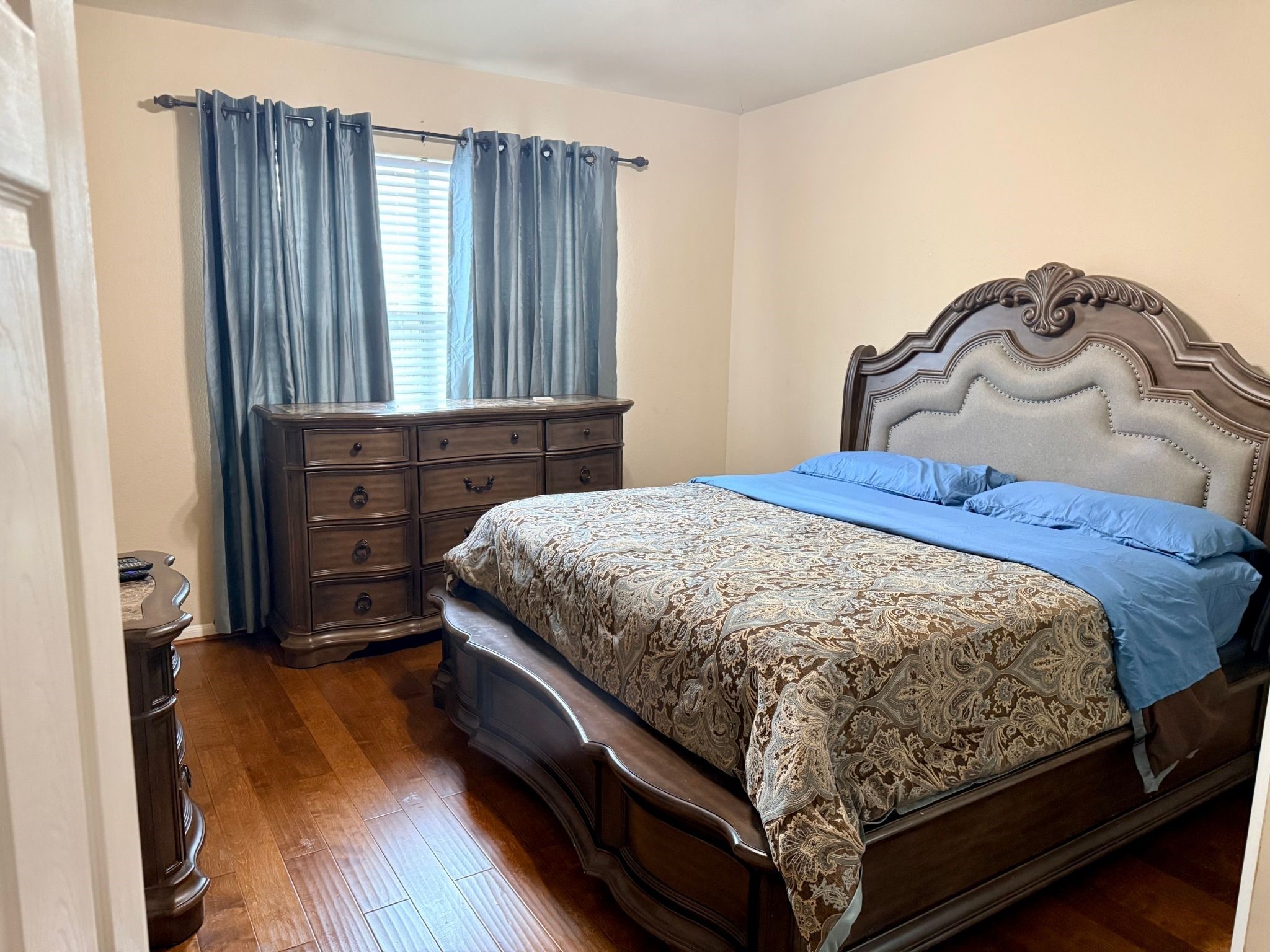 21831 Catoosa Drive Spring, TX 77388 - Photo 9 of 12 This cozy bedroom features warm wooden flooring and a large, ornate bed with matching dresser. The room is softly lit by natural light filtering through elegant curtains, creating a welcoming ambiance.