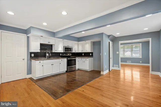 a kitchen with granite countertop a refrigerator oven a sink dishwasher and white cabinets with wooden floor