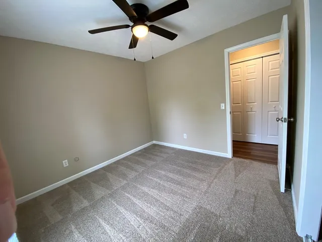 an empty room with a ceiling fan and carpet